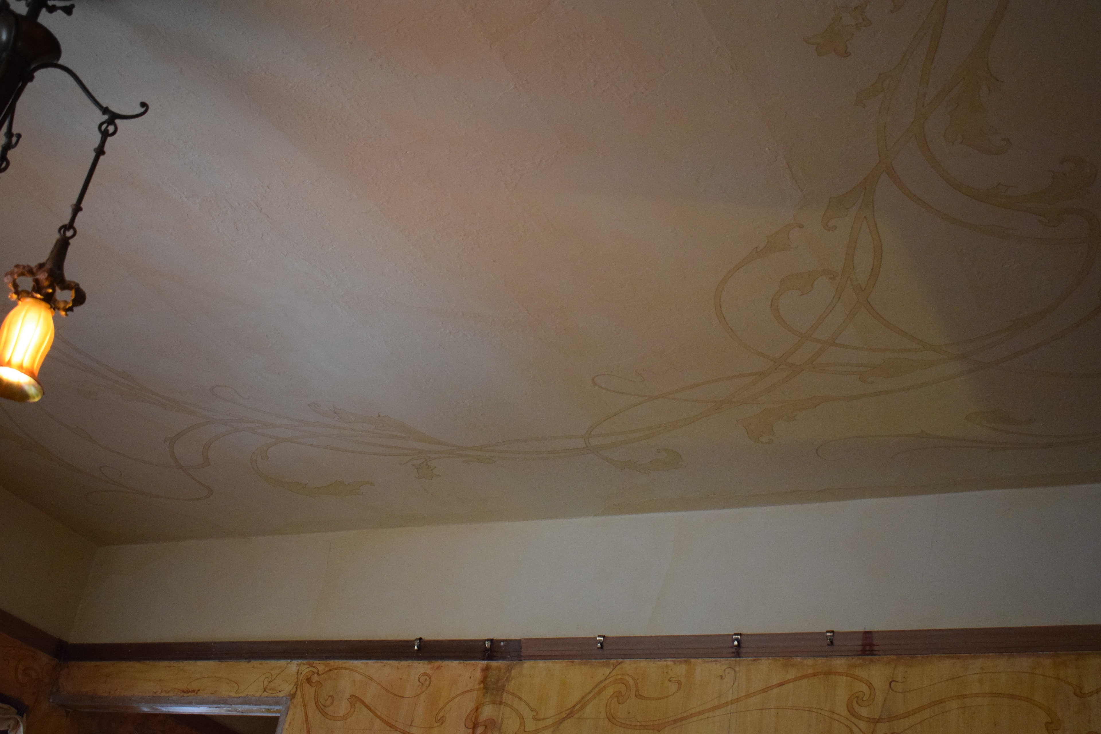 Art Nouveau ceiling with sweeping curvilinear ornament in warm gold tones, period pendant light fixture