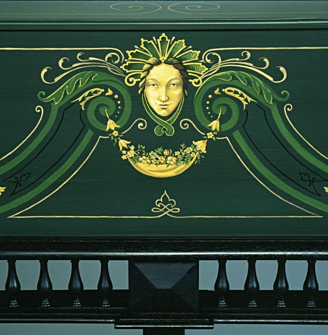 Close-up of the Vaudry 1681 apron — green ground with yellow and gold Daniel Marot-inspired scrollwork and a central female mask medallion